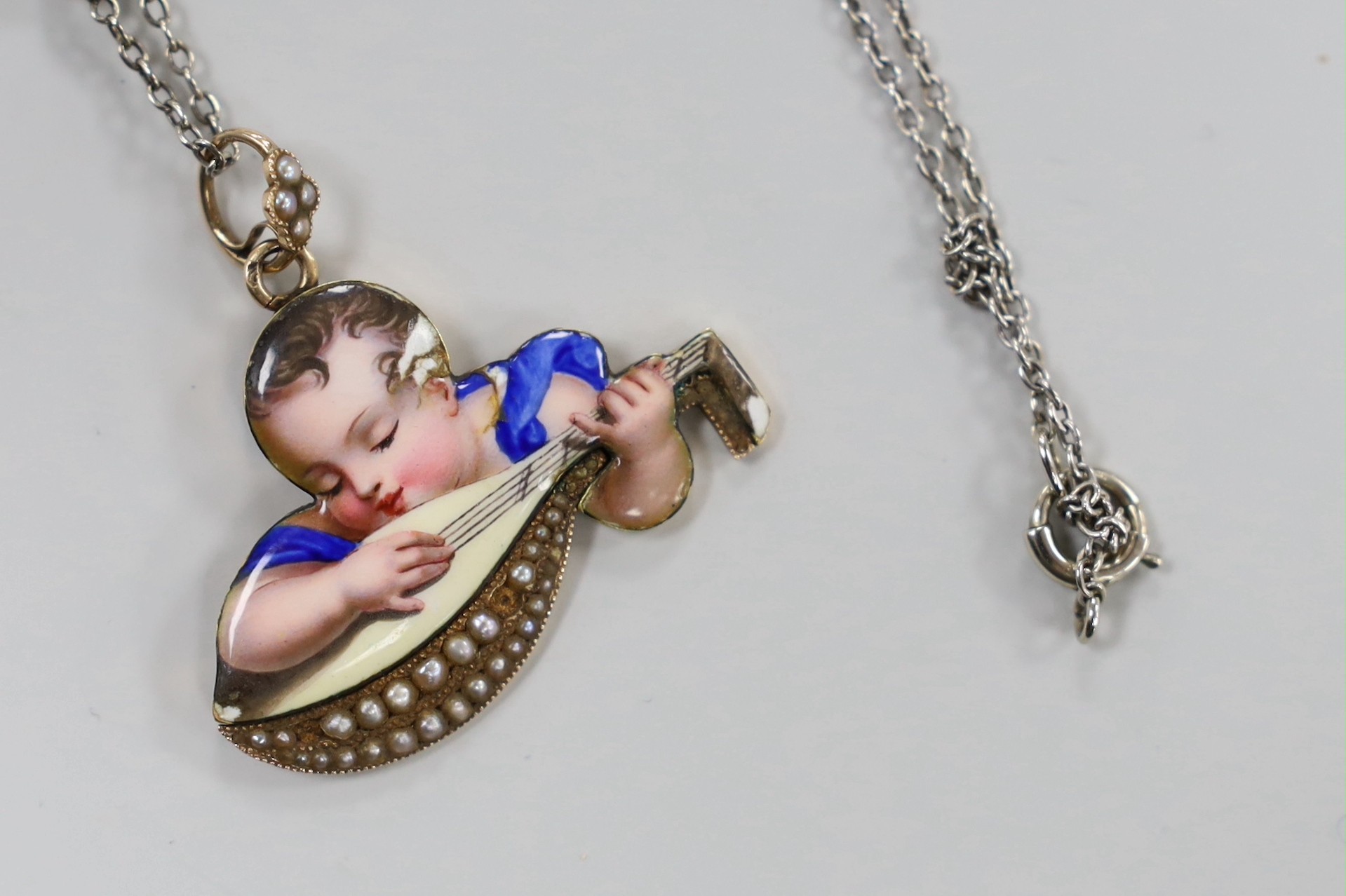 A continental yellow metal and enamel pendant, depicting a child with mandolin, 34mm, on a white metal and seed pearl chain, 38cm.